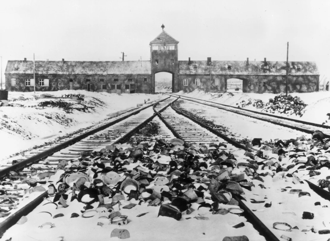 Schneebedeckte persönliche Gegenstände der in das Konzentrationslager Auschwitz Deportierten liegen auf den Bahngleisen, die zum Eingang des Lagers führen, auf einem Bild aus der Zeit um 1945.